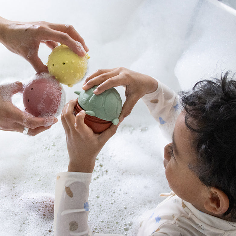 Kindsgut – Kind und erwachsene Person spielen mit Silikontieren im Wasser