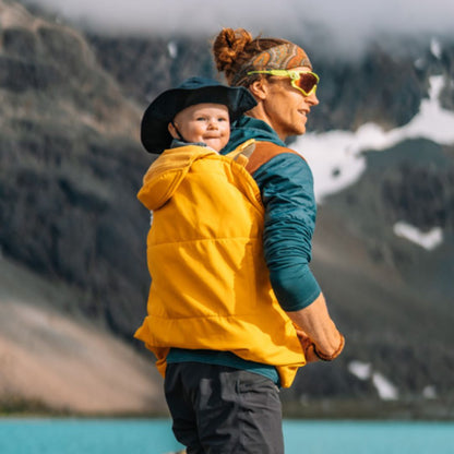 mamalila Softshell-Tragecover Allrounder – Person trägt Baby unter gelbem Cover auf dem Rücken