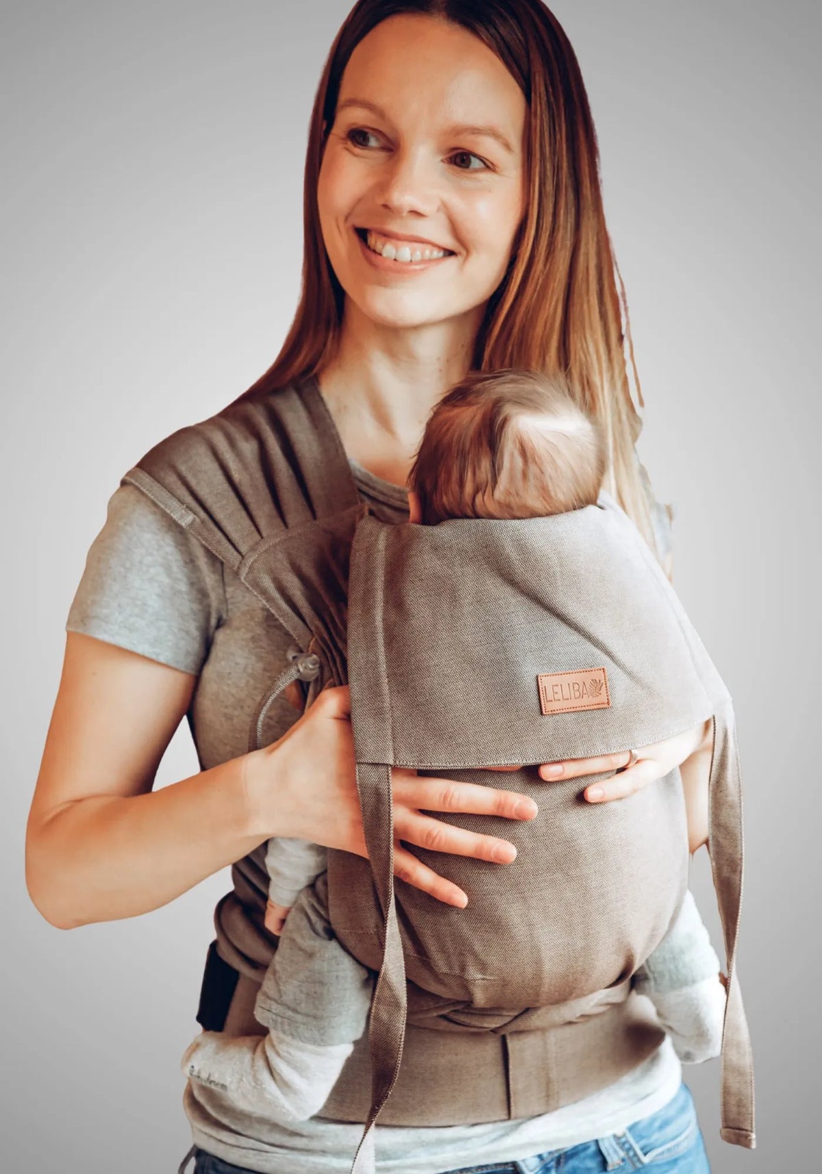 LELIBA Tai – Halfbuckle-Babytrage – Person trägt Baby in graubeiger Halfbuckle-Trage
