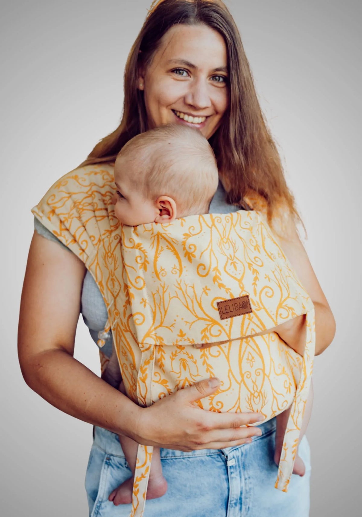 LELIBA Tai – Halfbuckle-Babytrage – Person trägt Baby in gelber gemusterter Babytrage